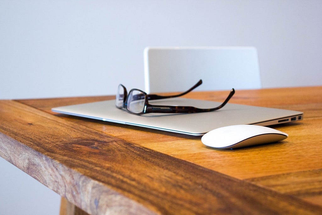 Eyeglasses on laptop and computer mouse on wooden table