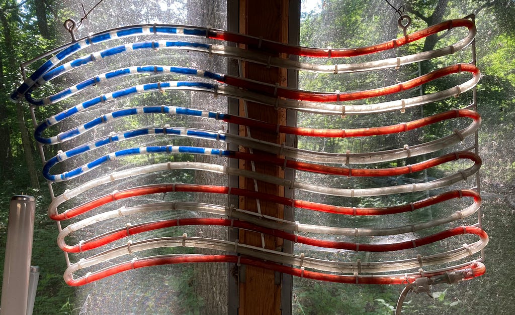 A neon American flag hangs in a window with both light and shadows passing through it.