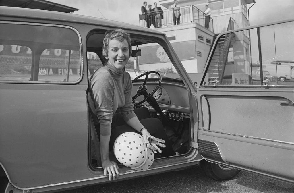 holding a polka-dotted helmet in her hand, a woman with a pixie cut smiles out of the window of a car