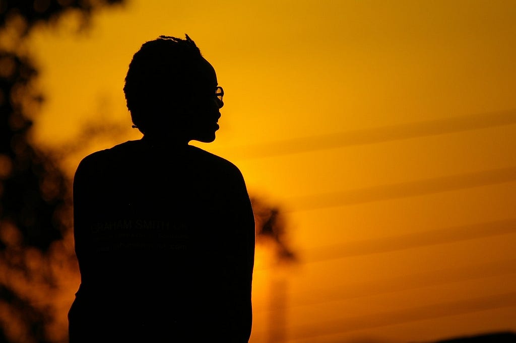 Black person’s silhouette sitting in front of sepia tone background.