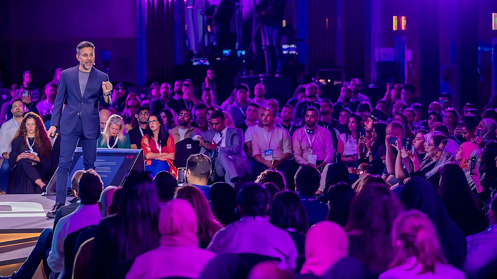 Vishen Lakhiani, an Indian entrepreneur and motivational speaker, addressing a large and engaged audience during a presentation on personal growth and self-improvement.