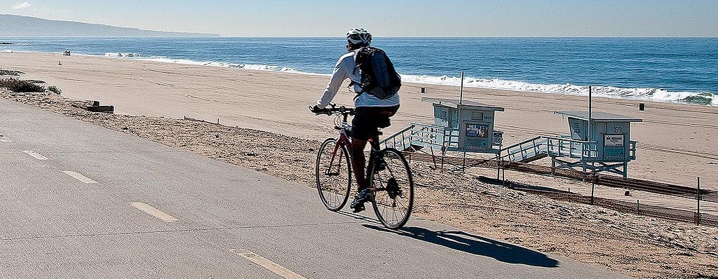 Los Angeles bike rider going down a road near the sandy Dockweiler State Beach