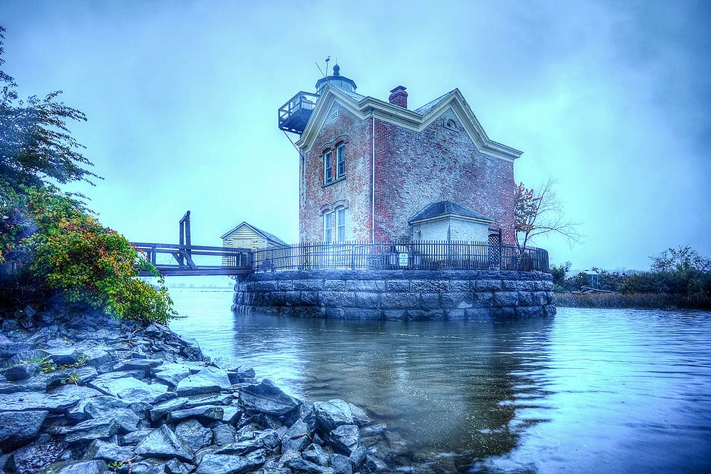 a two story red brick lighthouse on a river