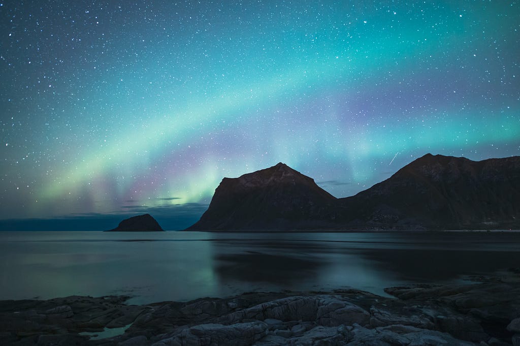 A Nordic starry night sky with aurora borealis, sea and a mountain siluette.