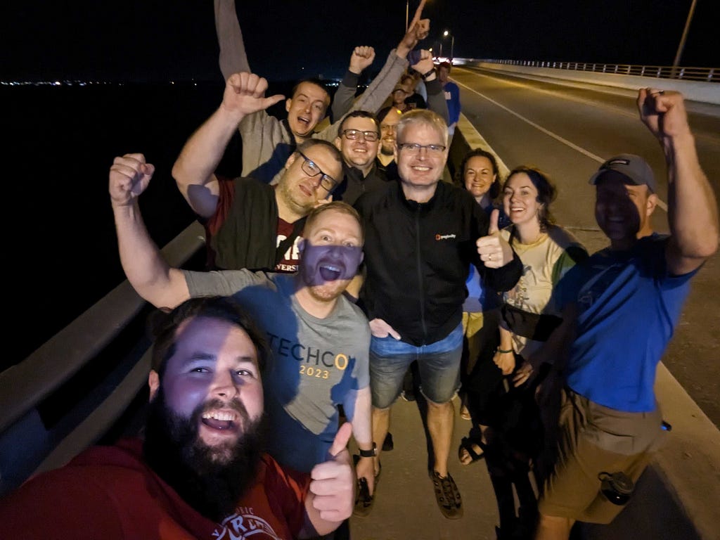 A group of people holds up celebratory fists or thumbs up as they stand on the side of a bridge.