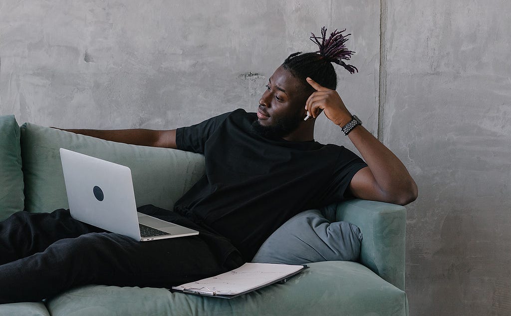 Image of a man laying on a couch working on his laptop