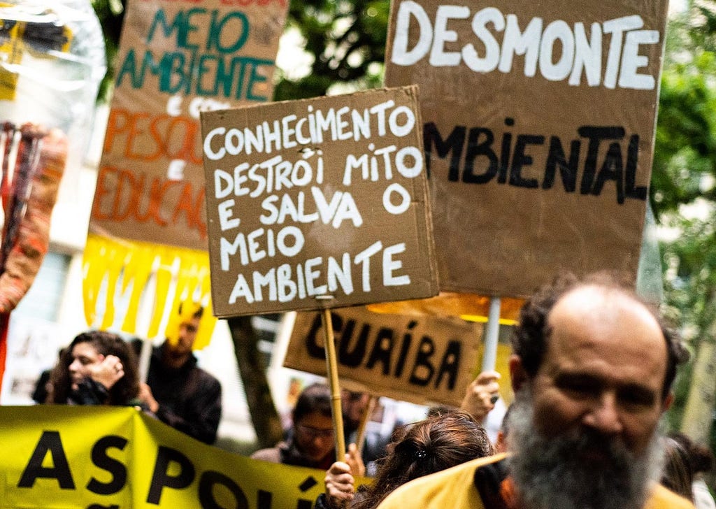 Manifestantes exibem cartazes com frases de protesto. Em destaque: Conhecimento destrói mito e salva o meio ambiente.