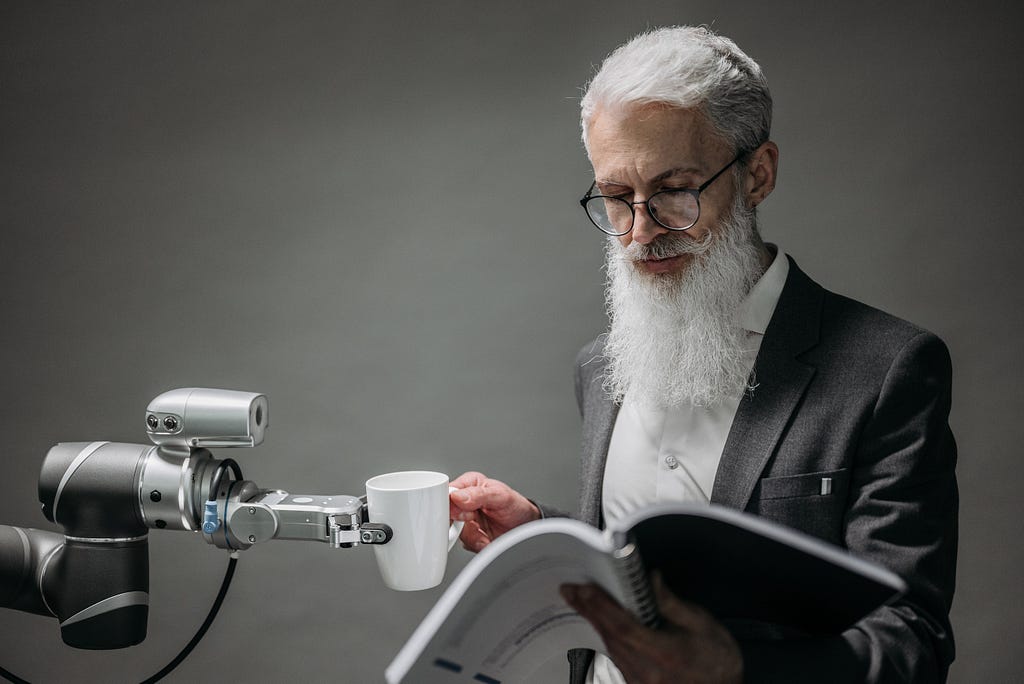 A person reads while a robotic arm hands them a cup.