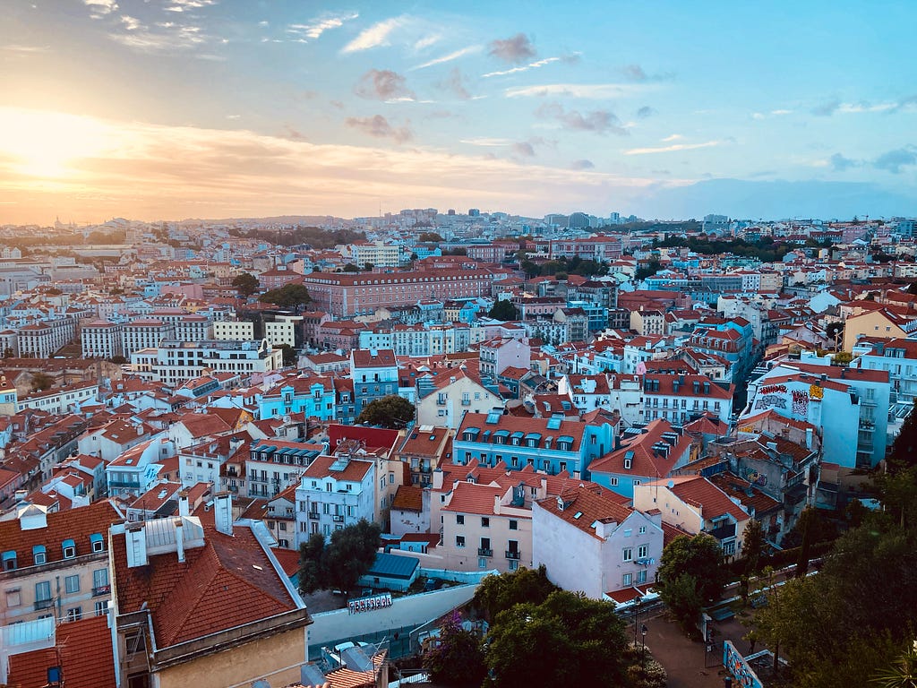 View of Lisbon, looking over the city center at dusk. The sun is setting and there are many houses with orange rooves.