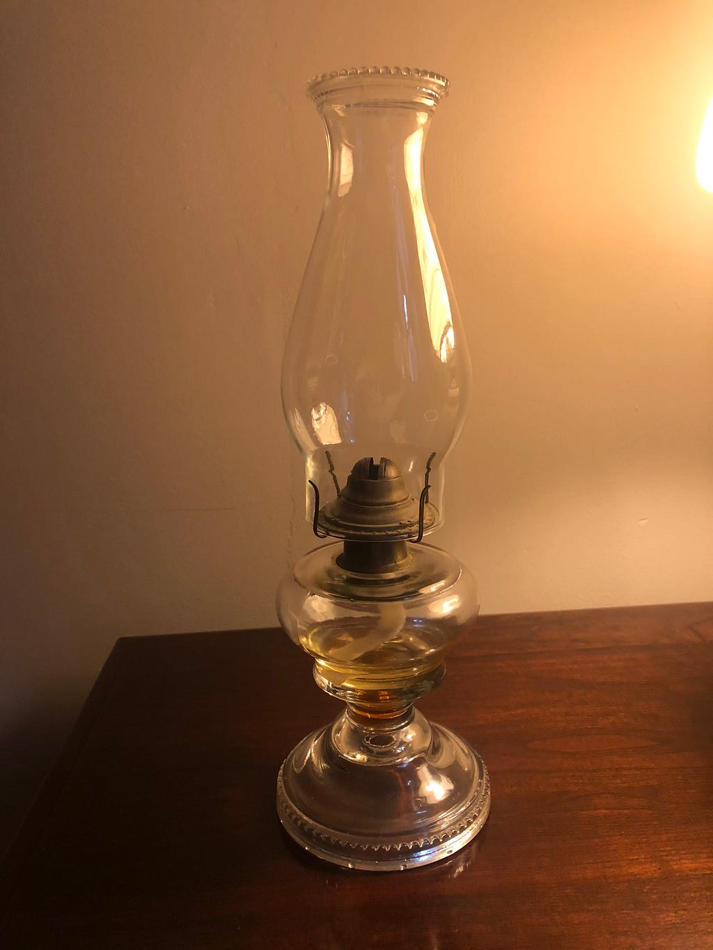 An oil lamp sits on a dark wood table against a neutral-colored while.