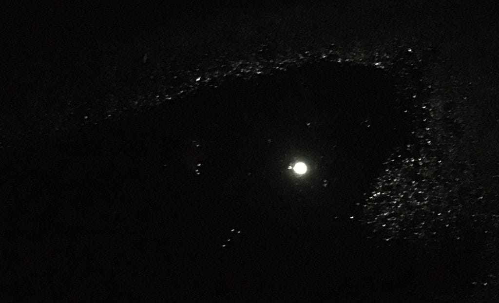 A dark rectangle with a scattered field of sparkles surrounding a puddle of water showing a reflected full moon