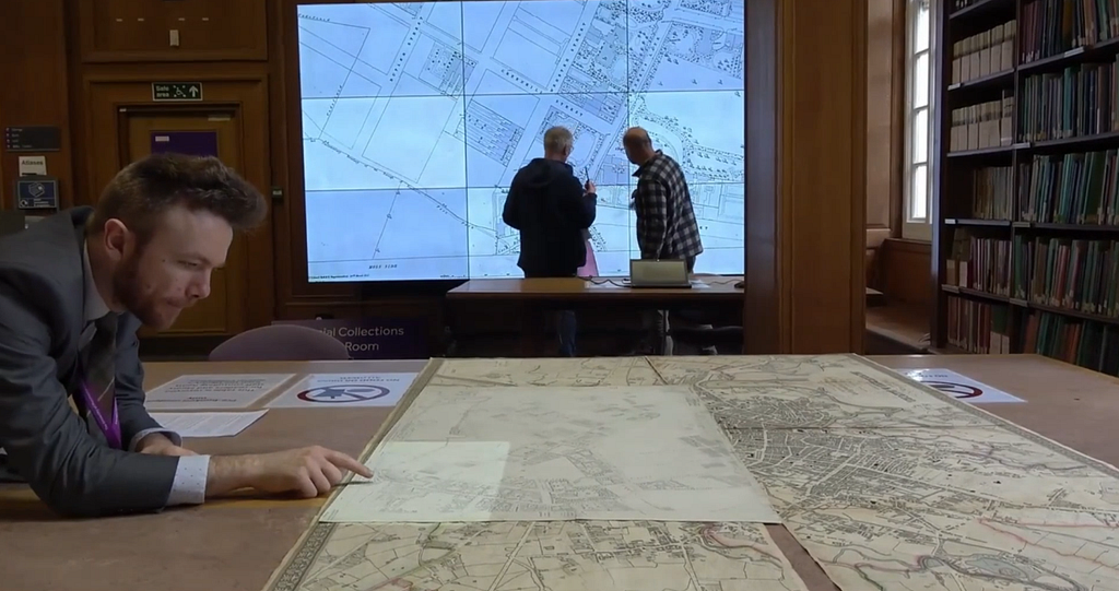 Three researchers looking at maps using a visualiser screen in the Special Collections Map Room at the Main Library, University of Manchester.