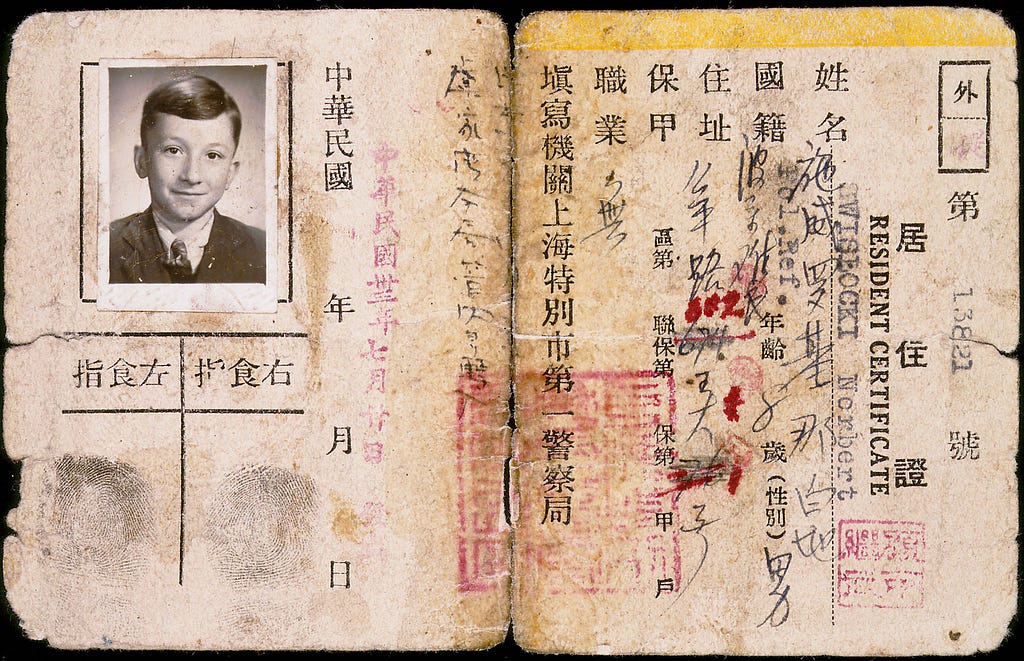 An unfolded document with ragged edges includes a photo of a young boy, two fingerprints, writing in characters, and red stamps. On the right, it says “RESIDENT CERTIFICATE.”