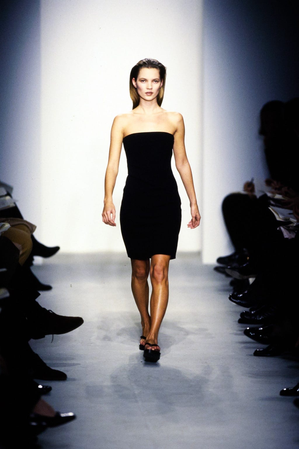 Kate Moss modeling a black tube dress on the runway.