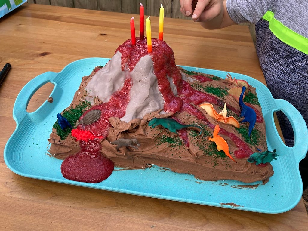A messy, but delicious sheet cake with an edible, erupting volcano and little plastic dinosaurs on top