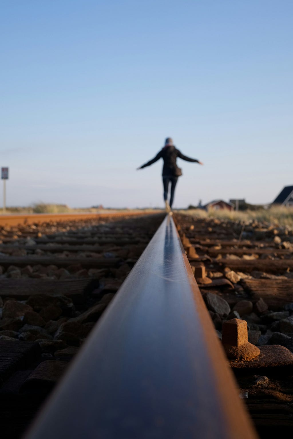 A person balancing on a railroad track against a bucolic background.