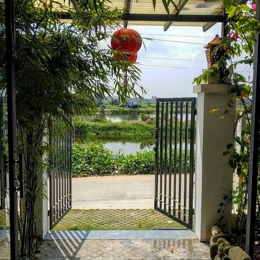 Open gates of a house in vietnam with a view of water and greenery