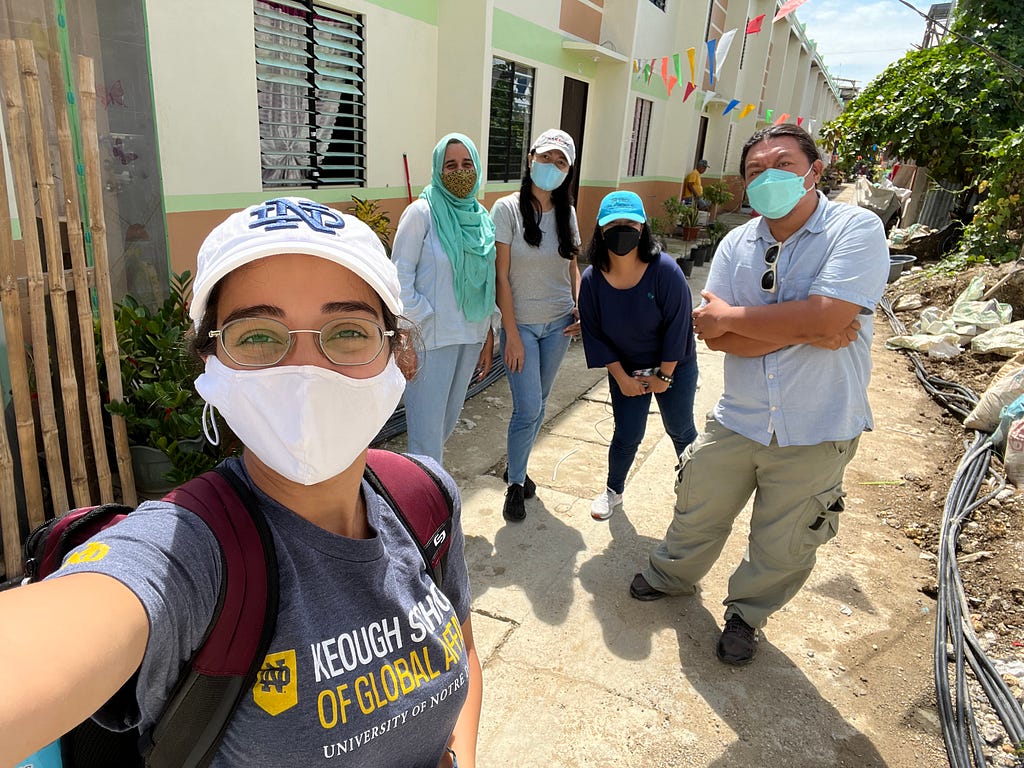 Marla with a white mask takinh a selfie with four other people wearing masks standing outside a building.