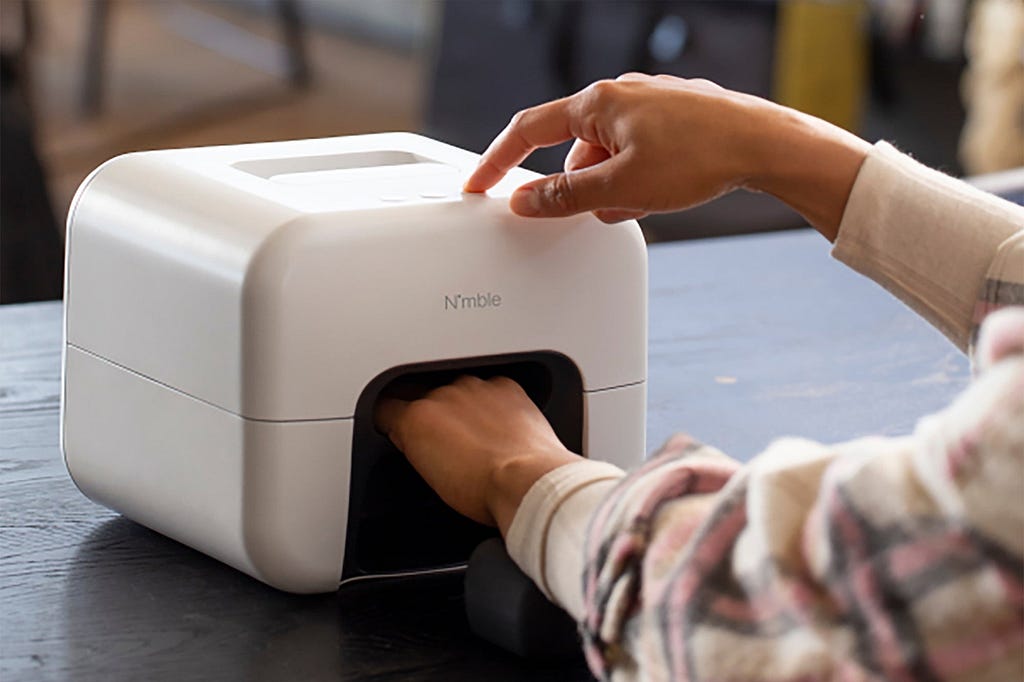 Someone inserting their hand into a toaster-sized computer vision-powered nail painting machine.