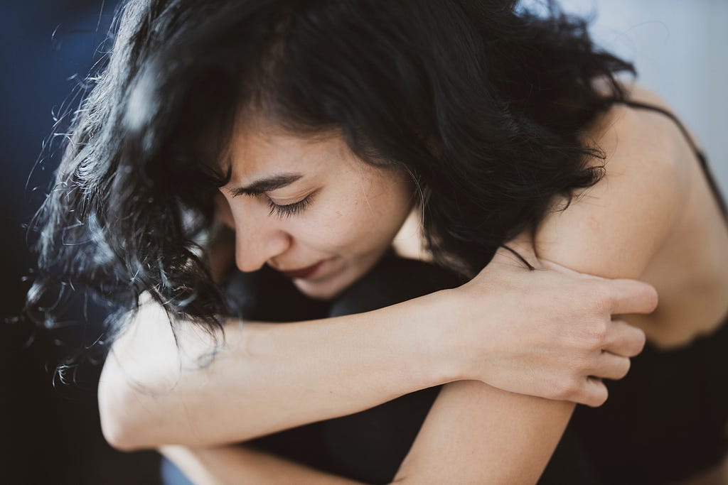 A young woman with a sad expression on her face hugging herself tightly.