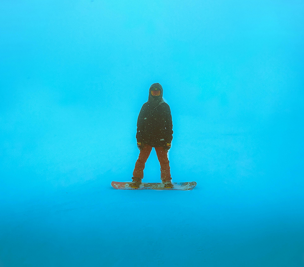 A snowboarder facing the camera amidst a blue-toned snowstorm.