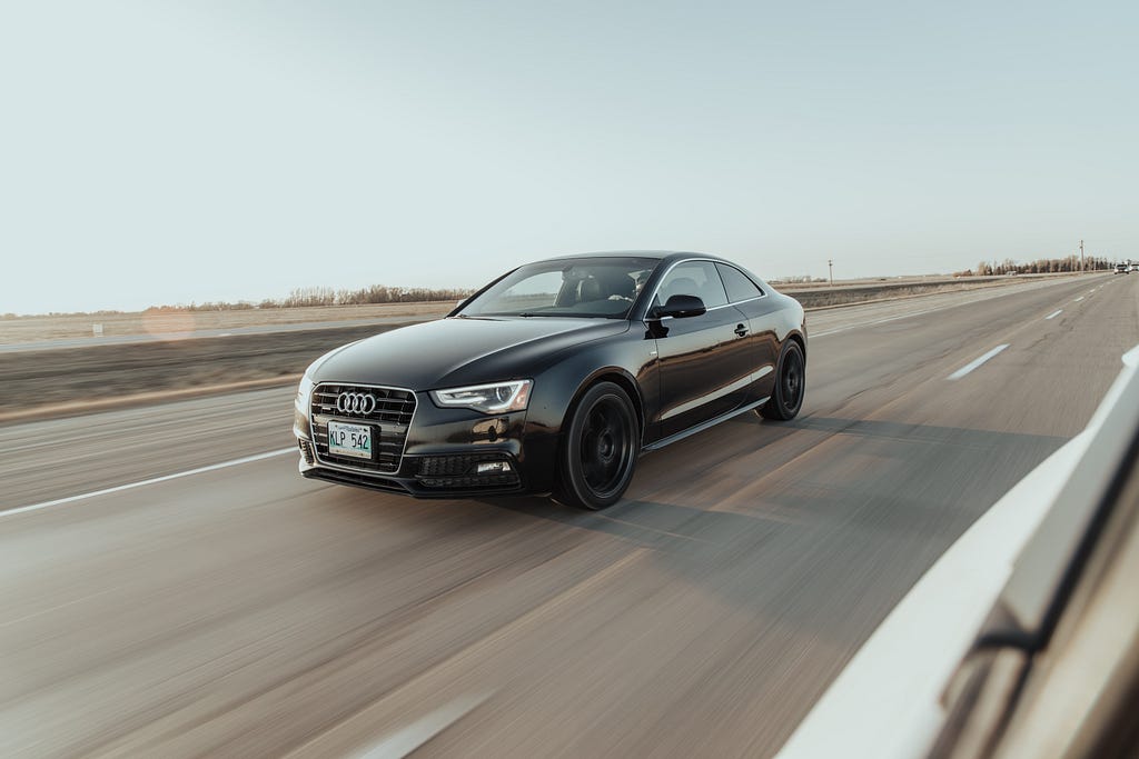 A black sedan speeds down an empty road