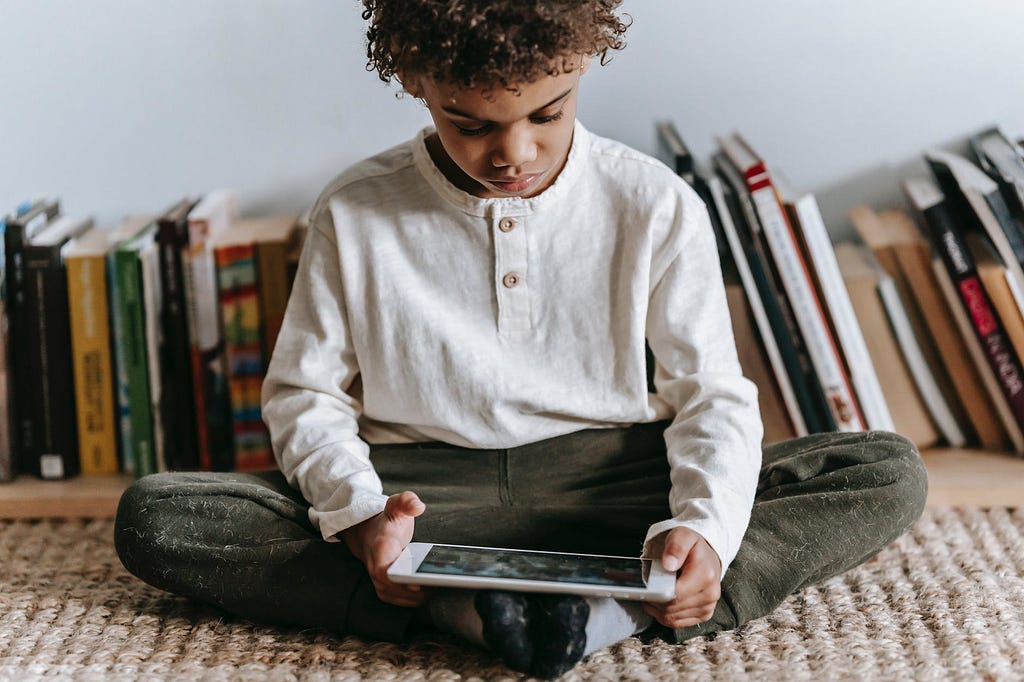 Child sitting in front of a row of books reading on a tablet