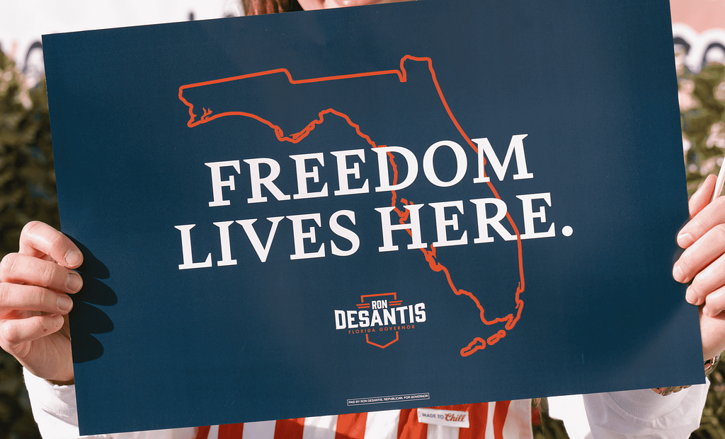 Photo of a red, white and blue campaign poster for Ron DeSantis for Governor of Florida that says “Freedom Lives Here” over an outline of the State of Florida