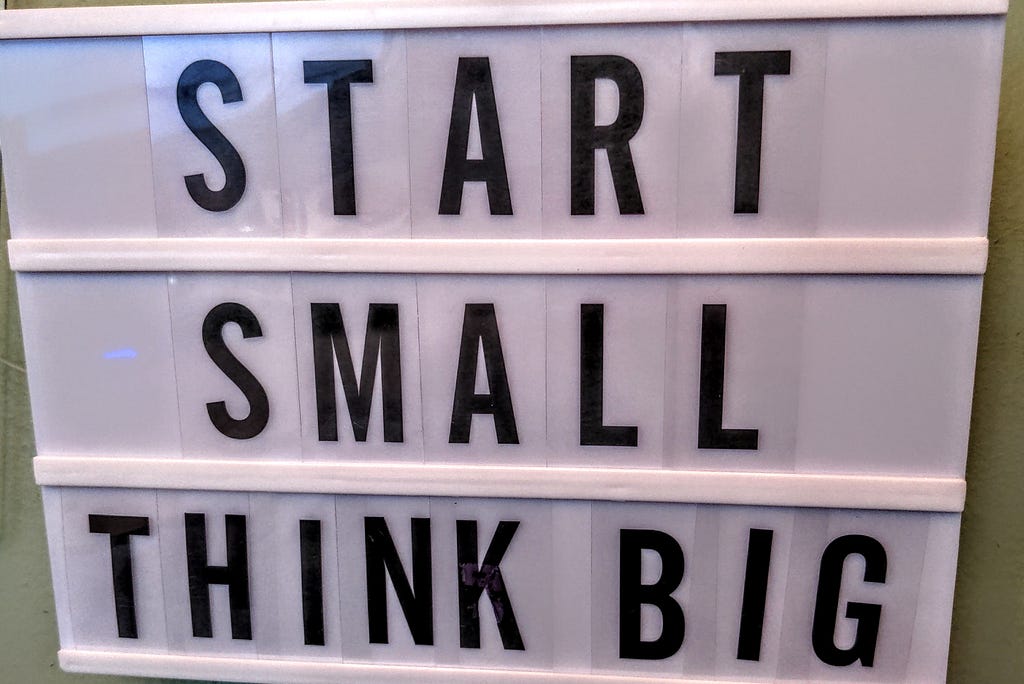 A white sign with moveable black letters that reads: “START SMALL THINK BIG”