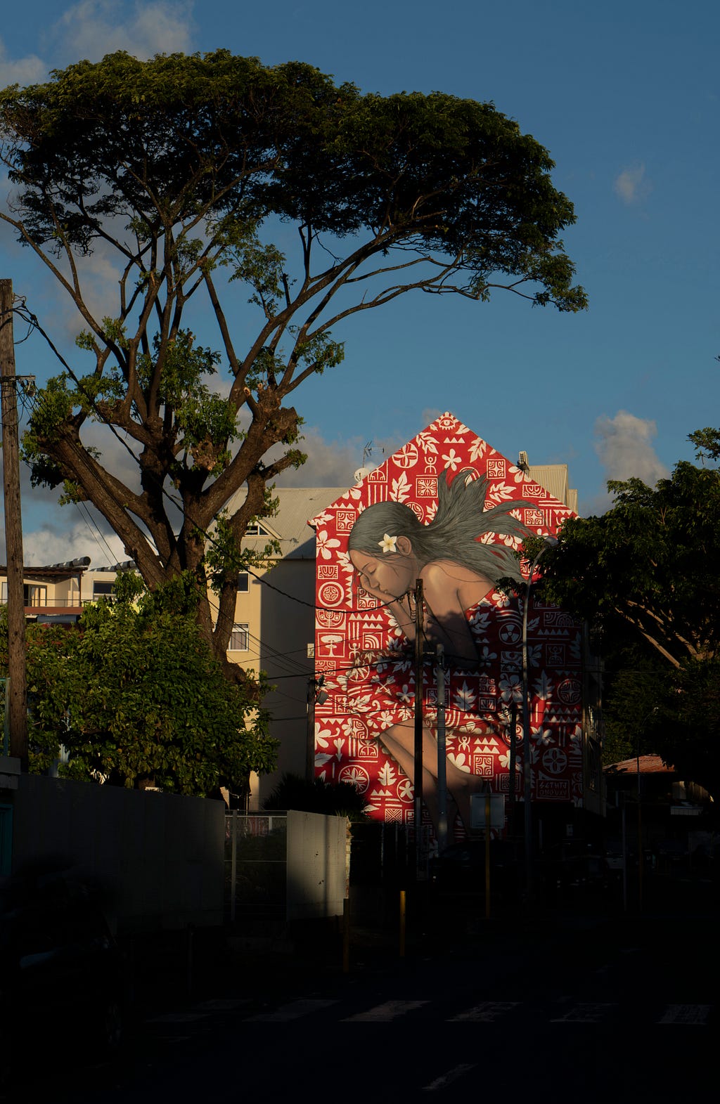 Photo of Tahitian urban landscape with trees and street art on the side of a building, photo credit Graham Clark