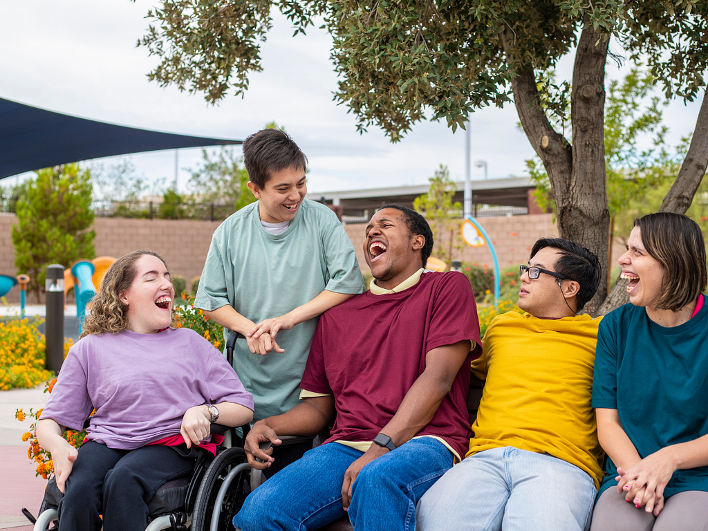 Five people sitting together, laughing. The first one, from left to right, is a wheelchair user.
