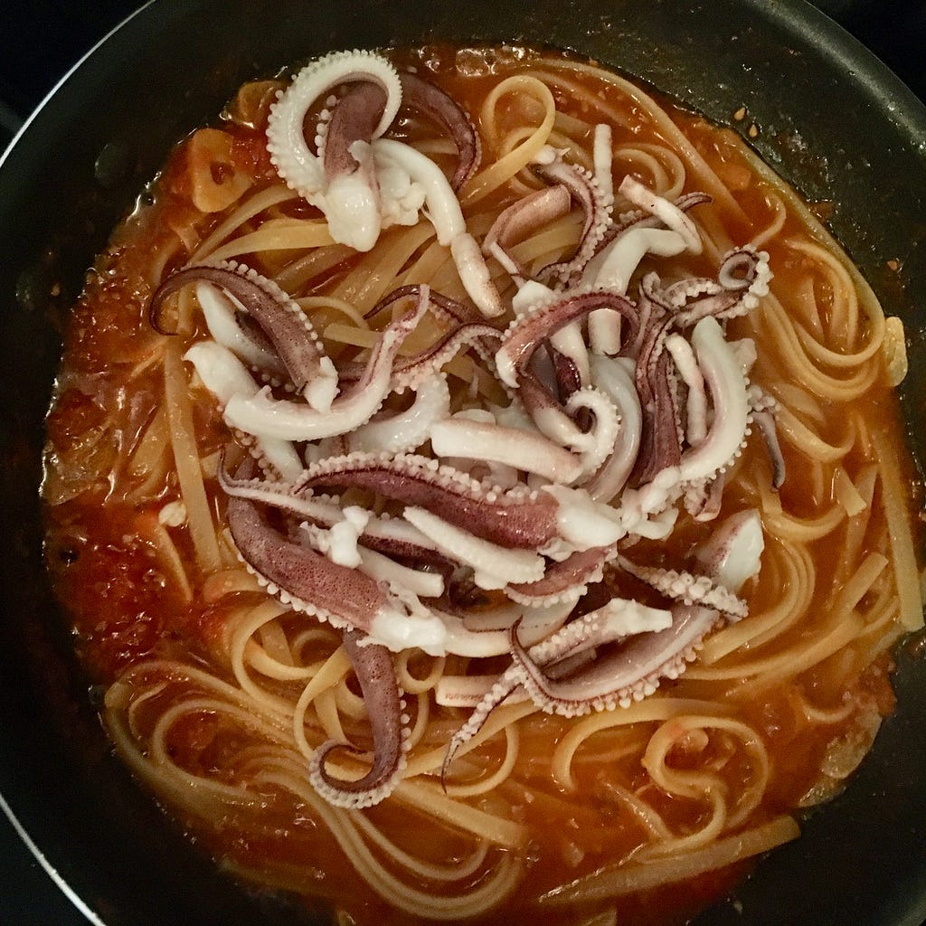 Overhead shot of a pan of linguini in sauce with squid tentacles on top.