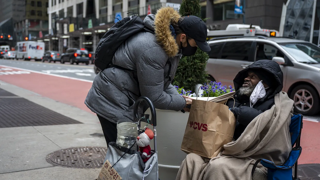 A passerby hands Anthony Lewis, a New Yorker experiencing homelessness, a bag filled with sandwiches and potato chips. (Photo: Hiram Alejandro Durán/THE CITY)