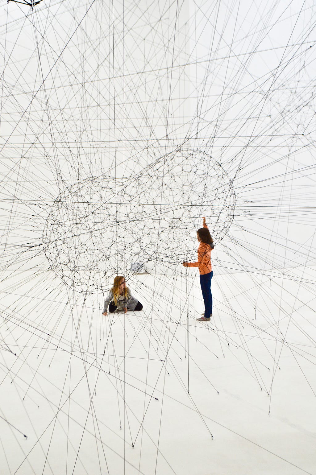 Two children play in an interconnected web of threads creating two colliding spheres with their interscetions.