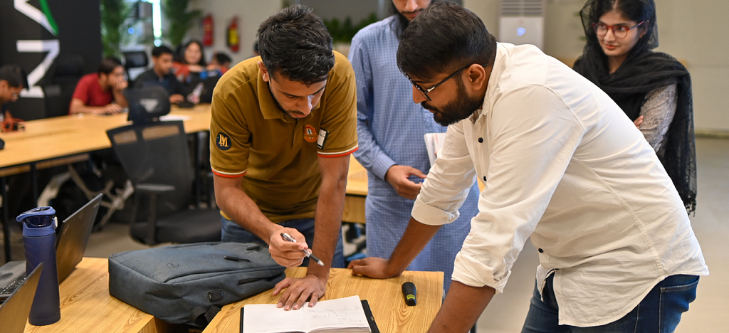 Two men figuring out a problem on a notebook.