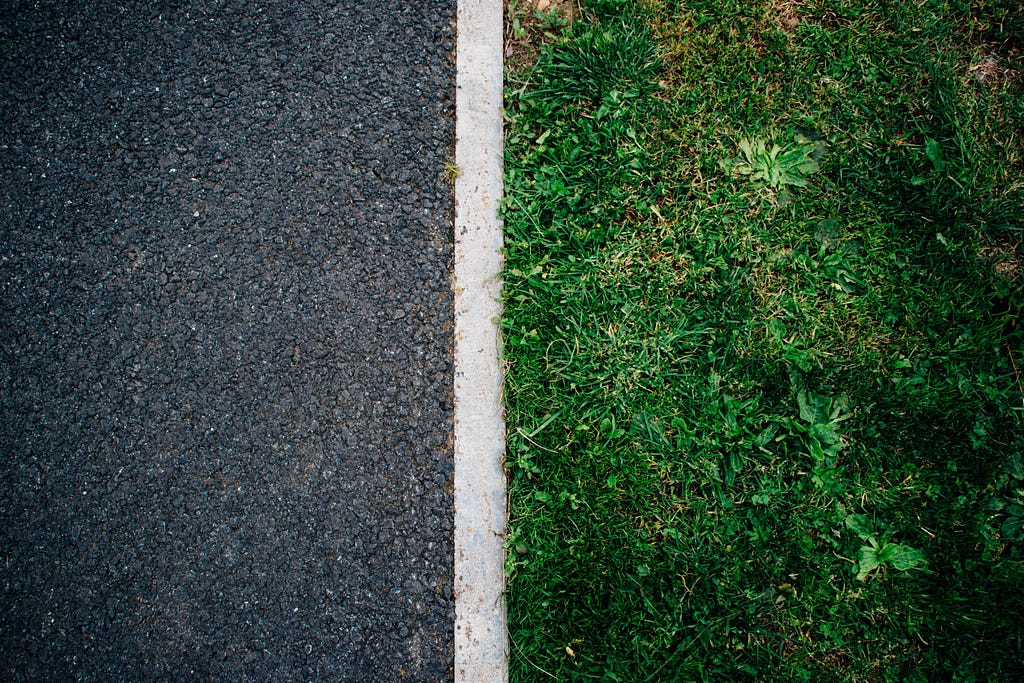 A concrete pavement situated next to green grass with a white line separating the two textures