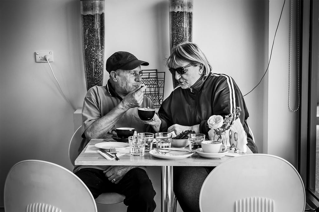 An older Italian couple sitting in a cafe eating pastries and drinking coffee, having fun. These are Stefani’s grandparents.