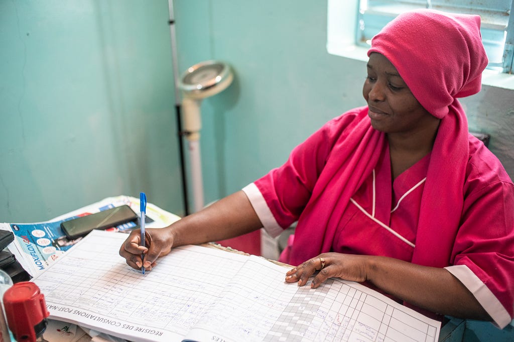 A health worker records a prescription for a new baby in a large book.
