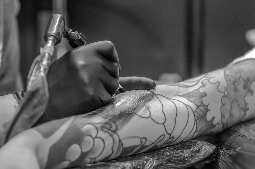 An arm sleeve tattoo being applied by an artist wearing black gloves.