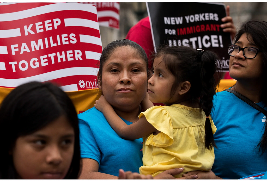 Keep families together. Immigrant poster reads behind gloomy looking mother holding a child in a protest