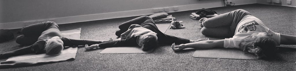 Several people lying on the floor in a yogic spinal twist posture.
