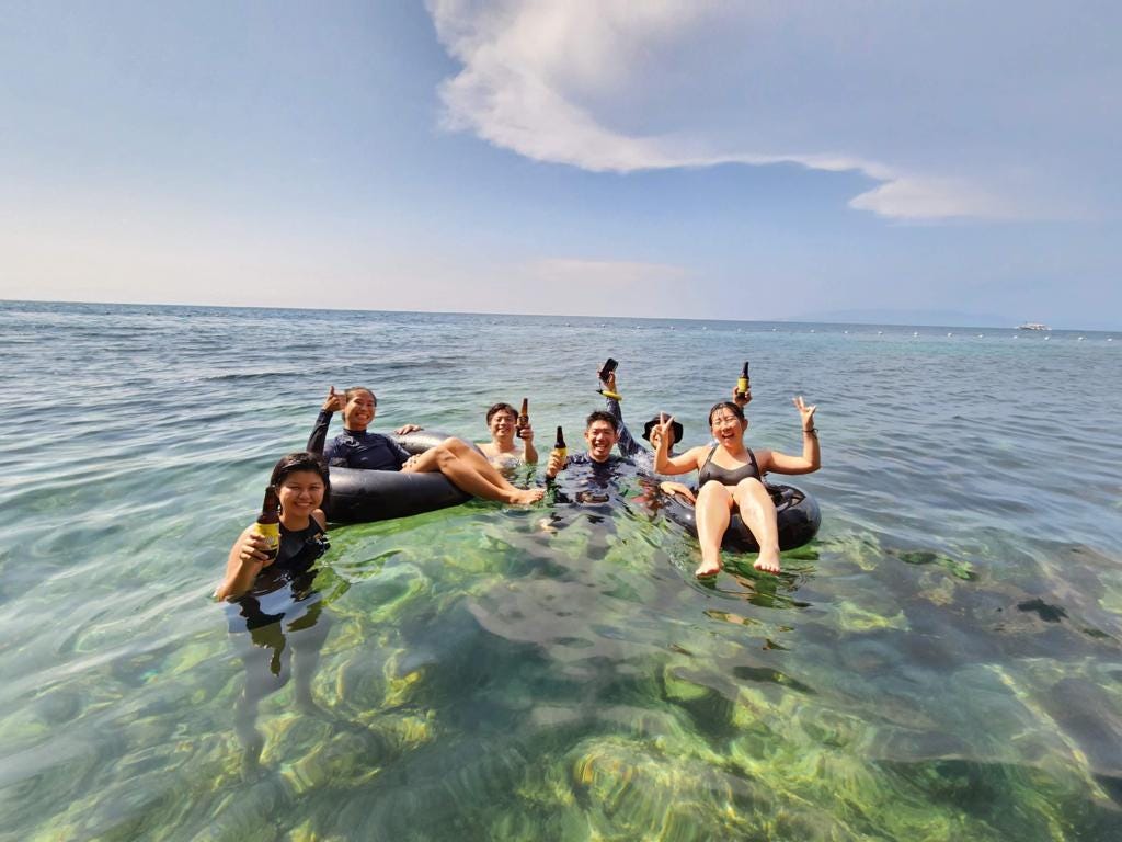 Six people relaxing in the clear waters of Napaling Reef in Bohol, Philippines with floaties and beers in hand.