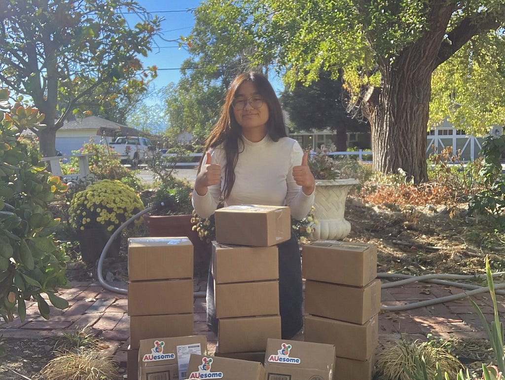 Anne stands outside with AUesome therapy kits in small cardboard boxes.