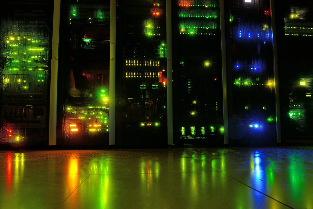 A photograph of a computer server rack line in operation with many differently colored activity lights shining