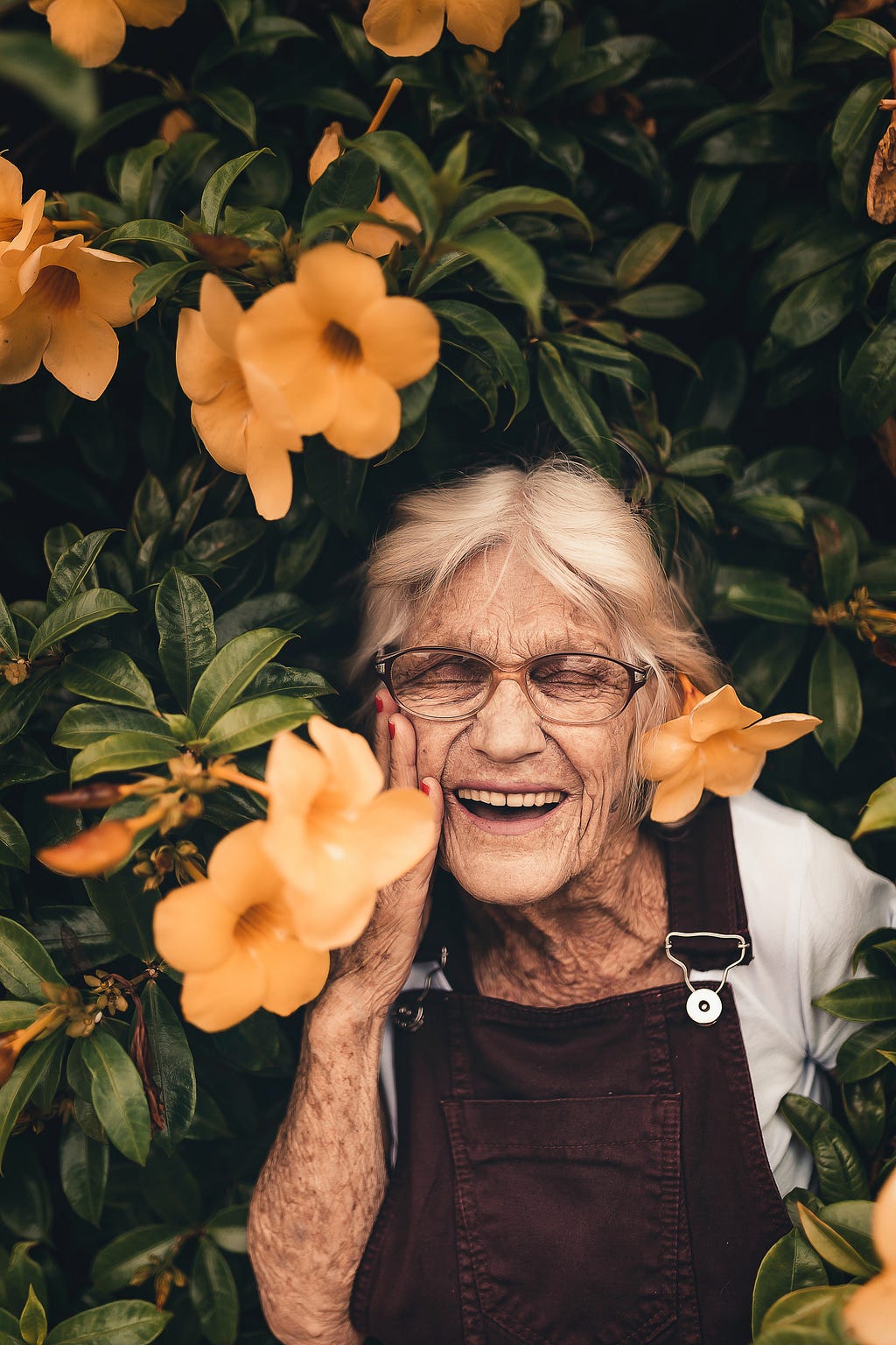 An elderly woman smiling standing in a tree with flowers surrounding her