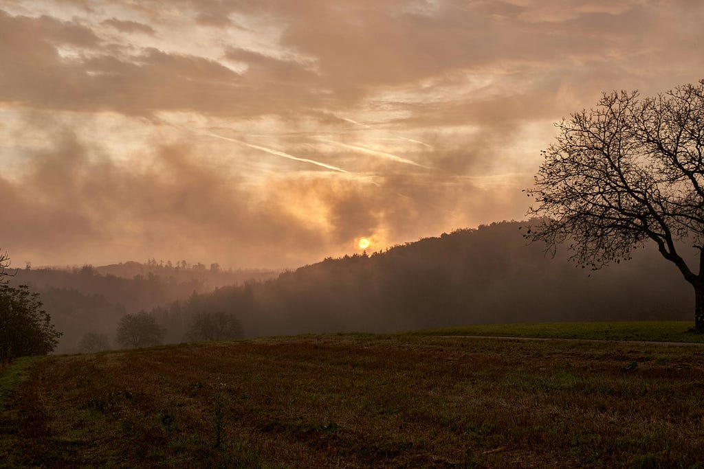 A foggy and cloudy rural landscape during sunset.