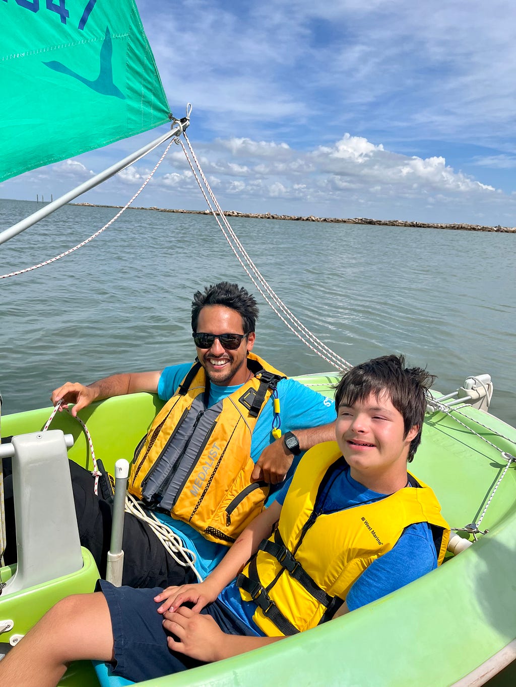 Word and camper smile at the camera while they are sailing in the sailboat in the bay.