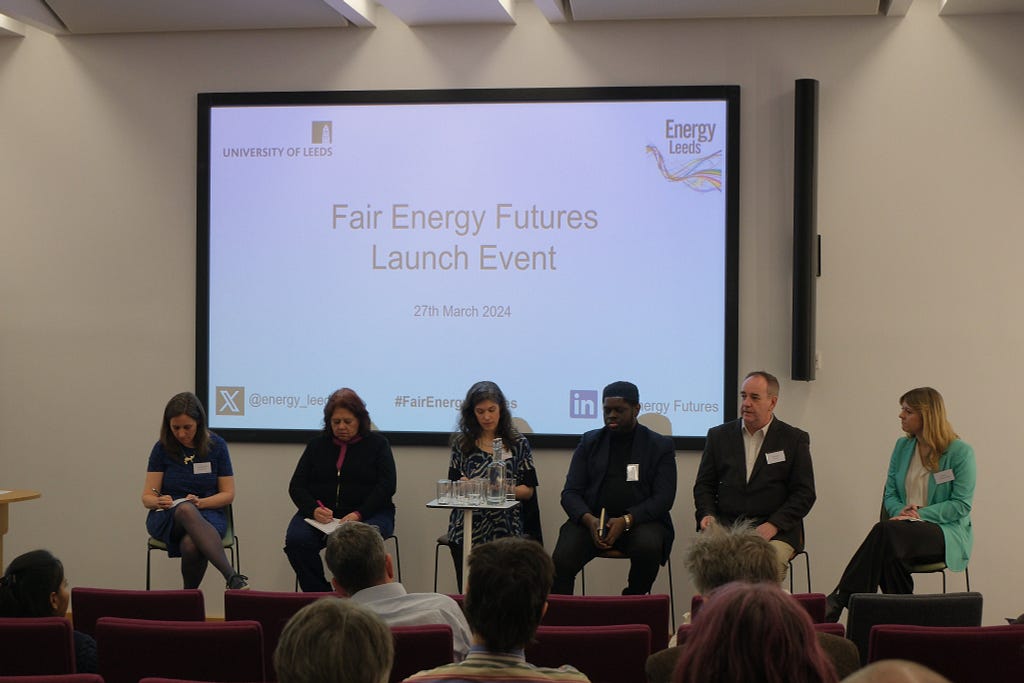 Panel of 6 speakers sat in front of a screen showing a slide titled “Fair Energy Futures Launch Event” taken from perspective of the audience.