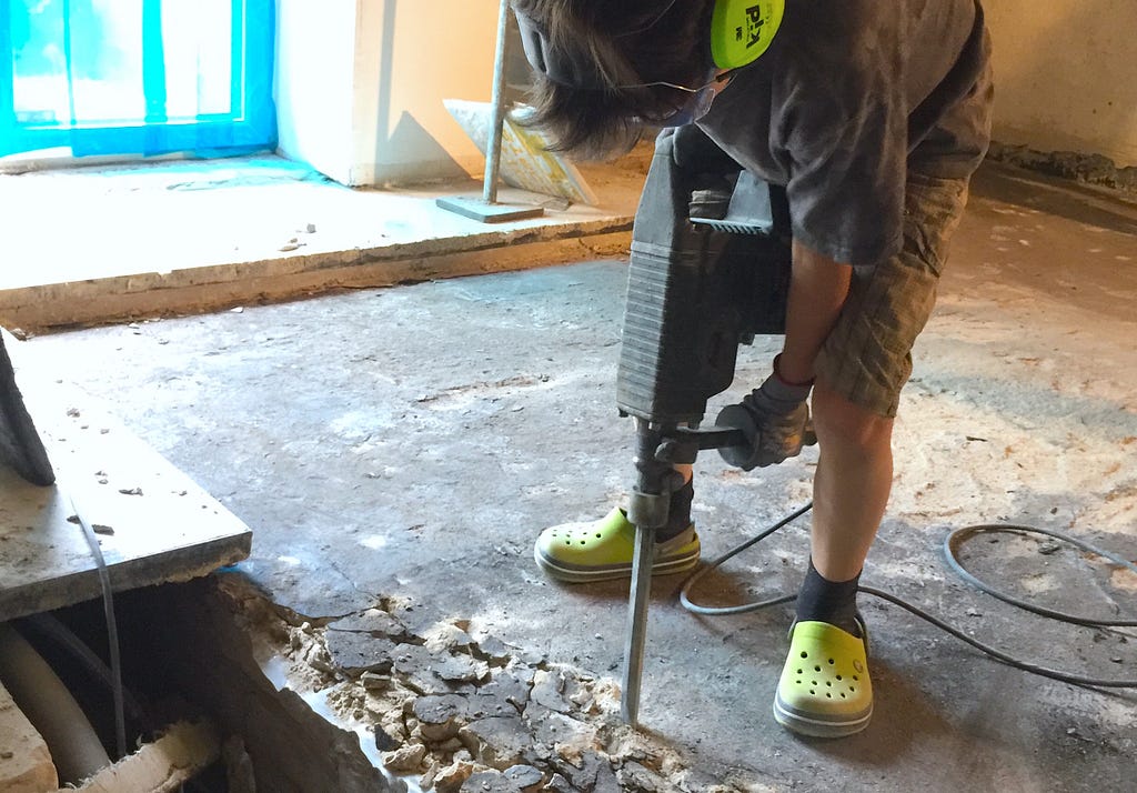 Ein Junge stemmt mit einem Bohrhammer den Fußboden auf