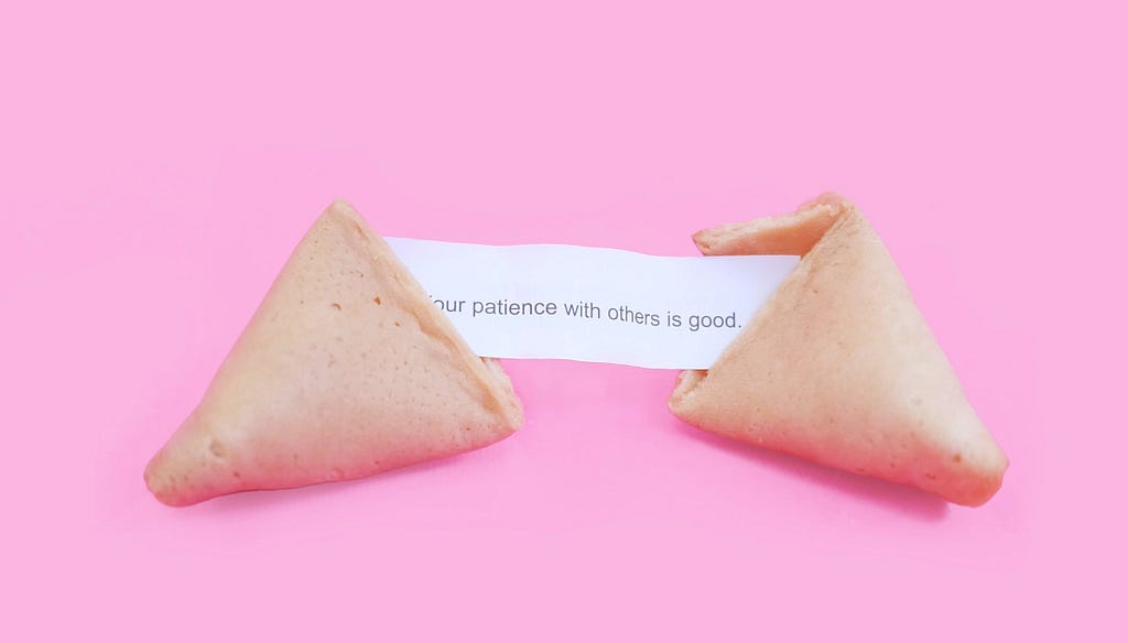 An open fortune cookie with a note inside saying: ‘Your patience with others is good’, on a bright pink background